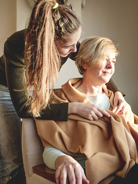 an older woman being wrapped in a 
blanket by a caregiver