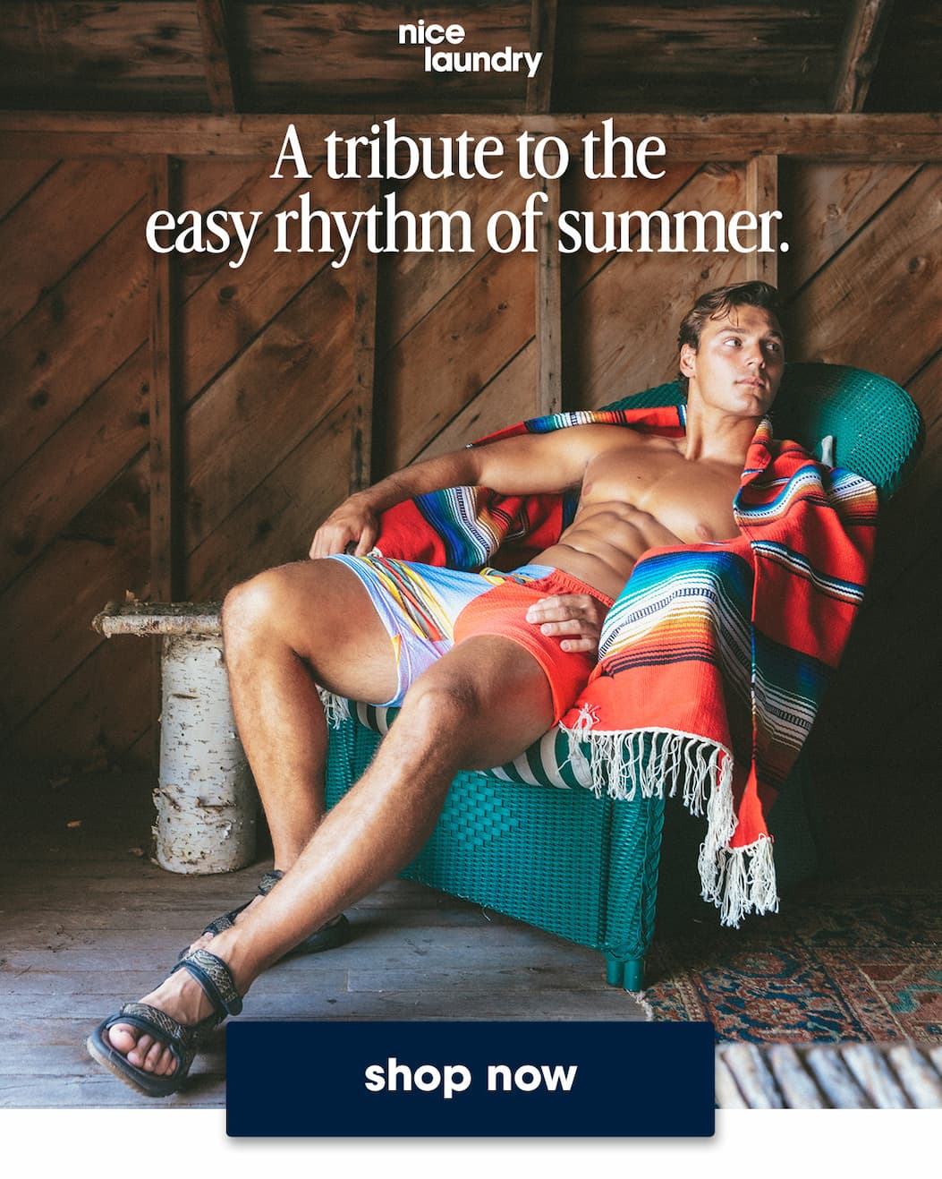 Shirtless man sitting in wicker chair and blanket wearing orange/blue/yellow stripe lounge short. Copy on image says "A tribute to the  easy rhythm of summer. shop now"