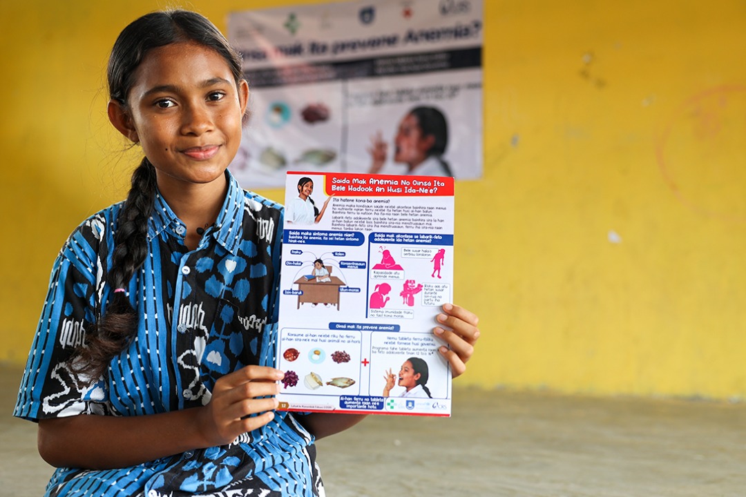 A girl holding an education poster about preventing anemia.