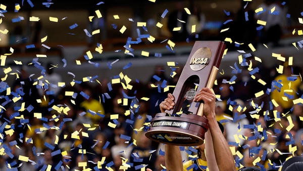 hands hold up NCAA Midwest Regional Championship trophy as yellow and blue confetti falls
