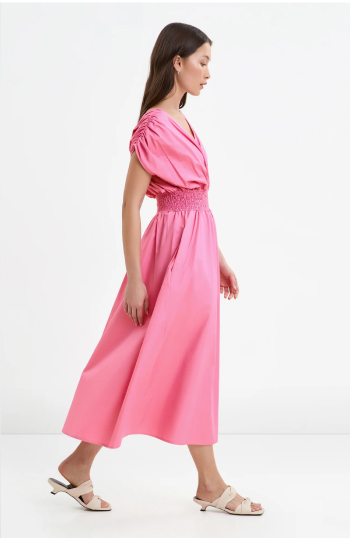 Yada in the Signe Dress with ruched sleeves and a smocked waist walks in profile against a white background.