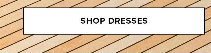 White 'SHOP DRESSES' button against a light brown diagonal wood plank pattern. Directs users to browse our current dress selection.