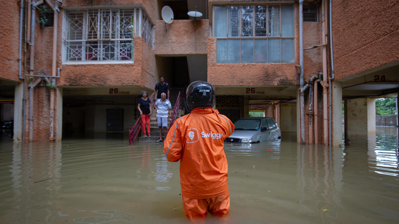 A Swiggy food delivery person wades through floodwaters to deliver an order.