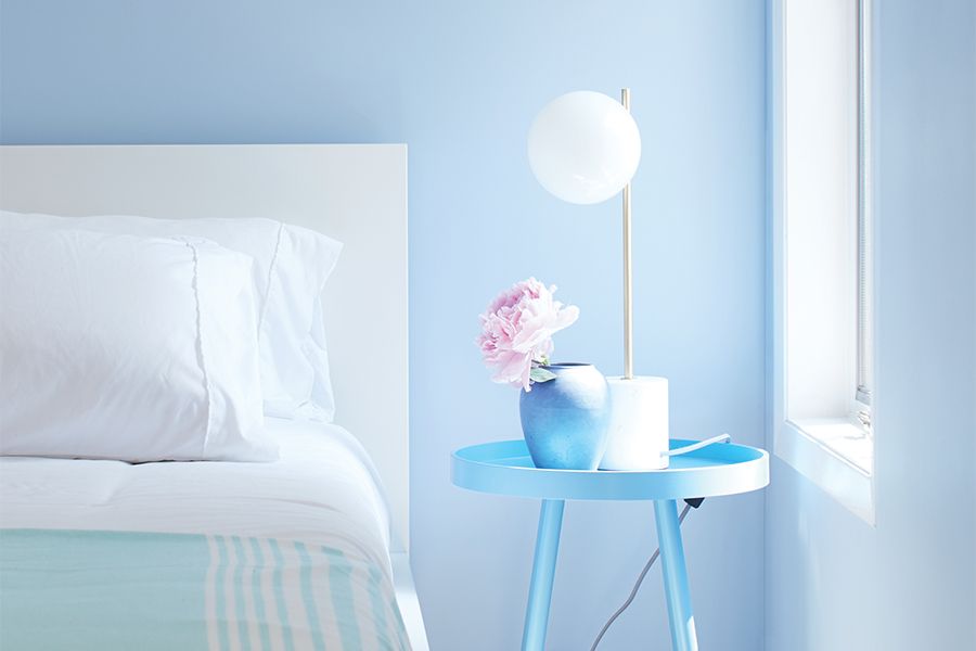 A blue-painted bedroom with blue and white bedding, light wood floors, and a blue night table.