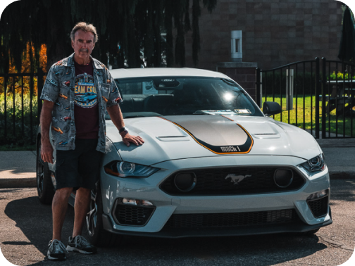 A parked Ford Mustang&reg; coupe with its owner standing beside it