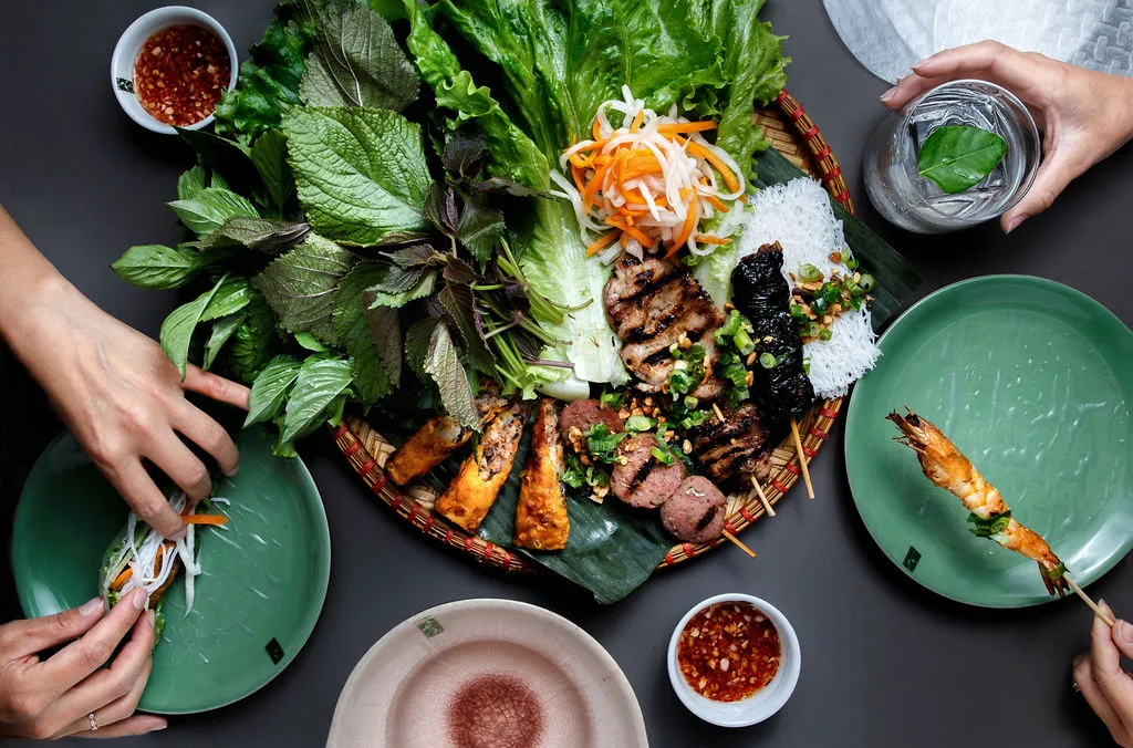 overhead shot of vietnamese street food plate with lots of herbs and skewers