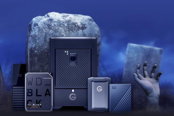 Collection of dark-colored Western Digital and G-Technology storage devices in a spooky, graveyard-like setting with tombstones and a hand reaching up from the ground, under a dark blue sky.