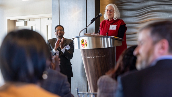 Anne Simon speaks at podium, with President Pines at left