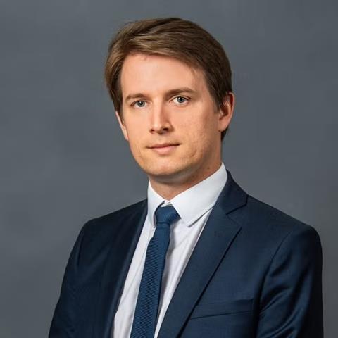 Professional headshot of a person in a suit before a grey background.