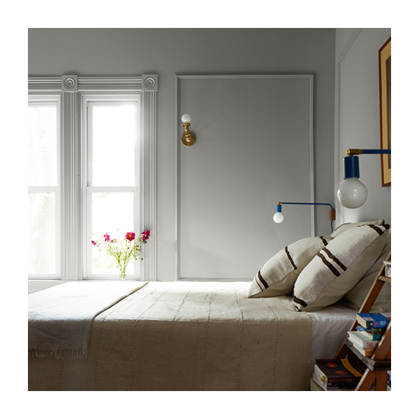 Greige-painted bedroom with molding, simple bedding, tiered end table, flowers, and Edison wall sconces.