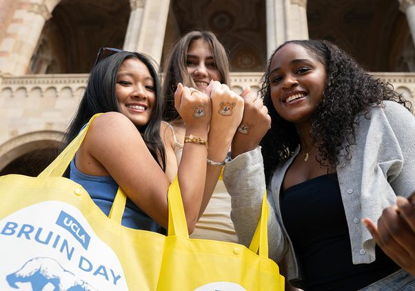 Three smiling students hold up their fists to display matching UCLA Bruin bear temporary tattoos on their hands during UCLA Bruin Day