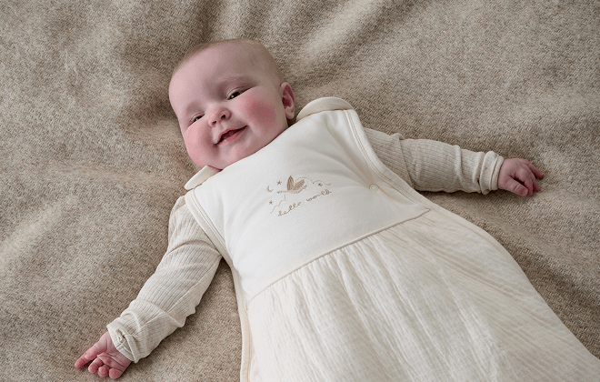 Baby lay, smiling, wearing duckling style dreampod sleep bag