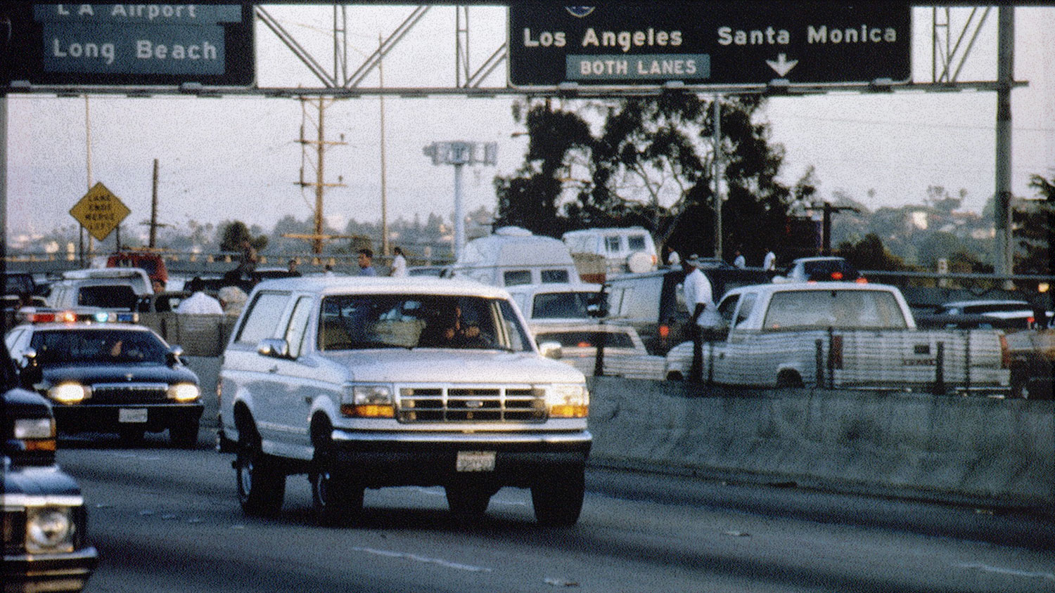 A white truck drives down the highway followed by police cars.