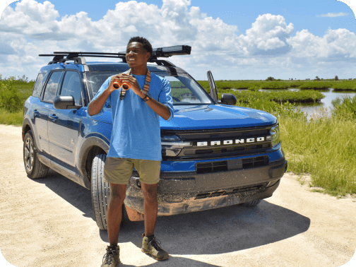 A man holding binoculars and standing in front of a parked Bronco&reg; Sport SUV