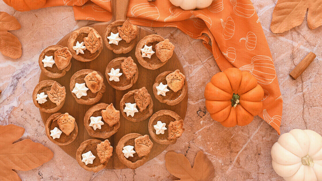 Circular dish full of little pumpkin tarts. There are a couple small pumpkins to the right side.