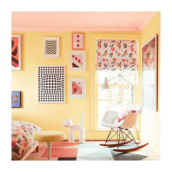 A bright, cheerful kid’s bedroom with yellow painted walls, a pastel pink ceiling, colorful framed artwork, modern furniture, a multicolor bedspread, and geometric print rug.
