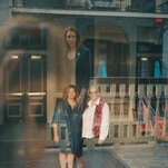 An image of Laura Oswald and Christine DeGrange standing side-by-side, as seen through a window, with a reflection of Susan Saulny.