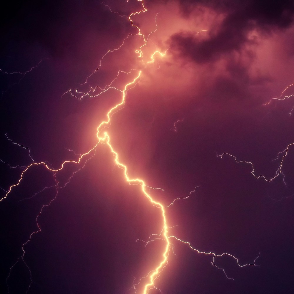 Orange-tinted lightning forks through dark red clouds.