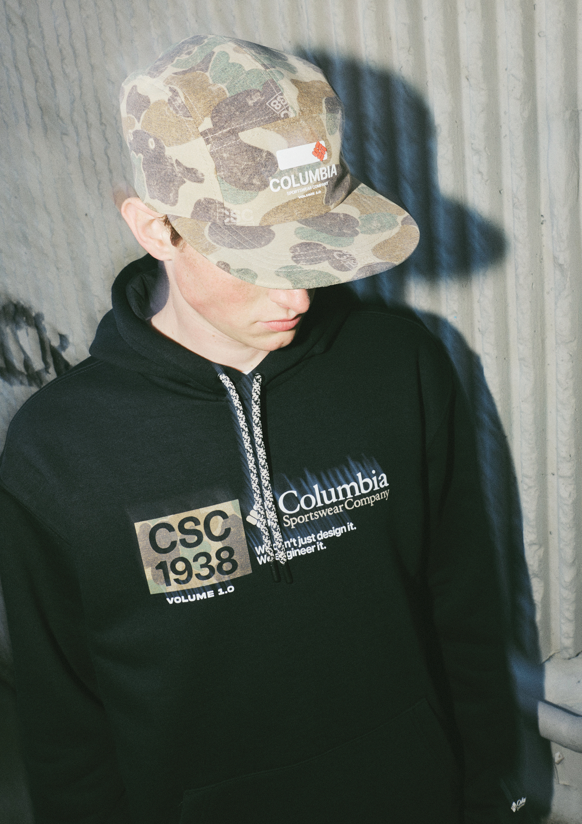 Man in CSC1938 camo hat and black hoodie, facing down to show hat logo and top of bill.