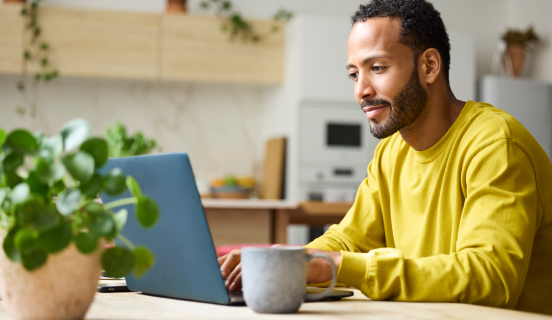 A man sits at a kitchen table and types on a laptop.