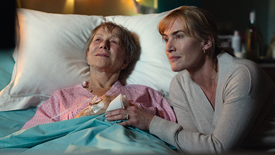 A woman holds the hand of another woman in a hospital bed.