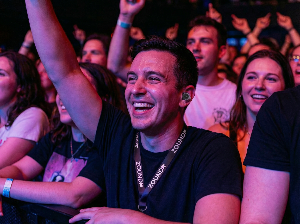 Man wearing Zound earplugs at a concert, front row, smiling