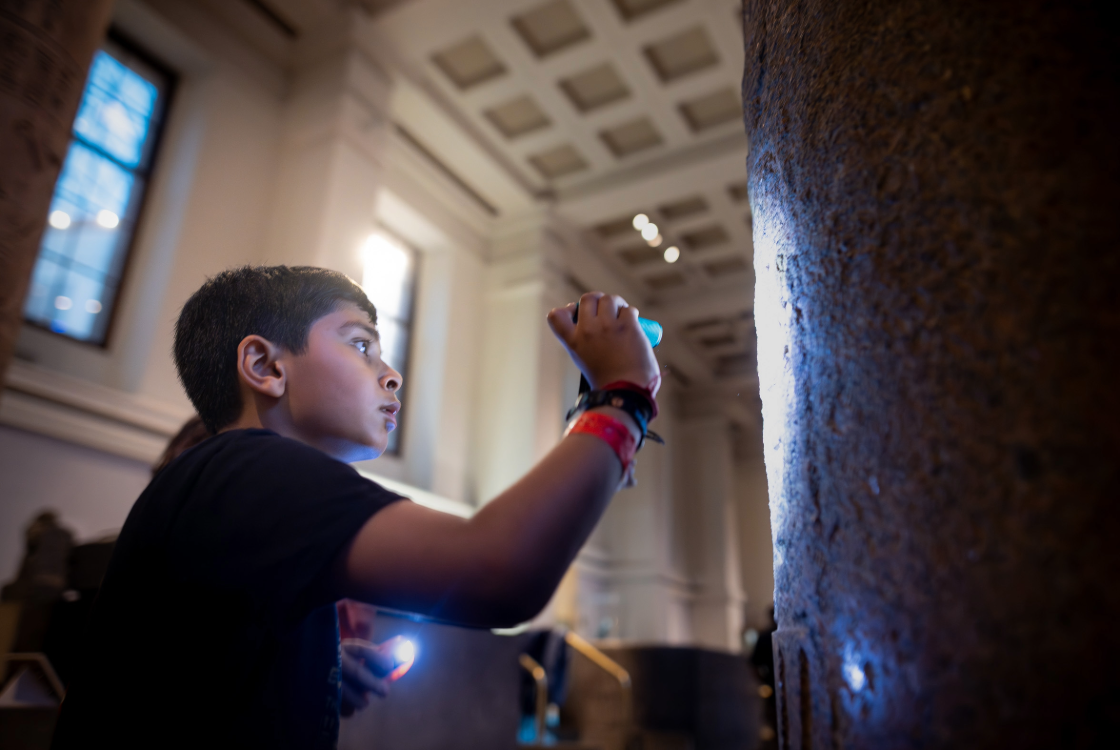 Child closely looking at stone object with a torch.