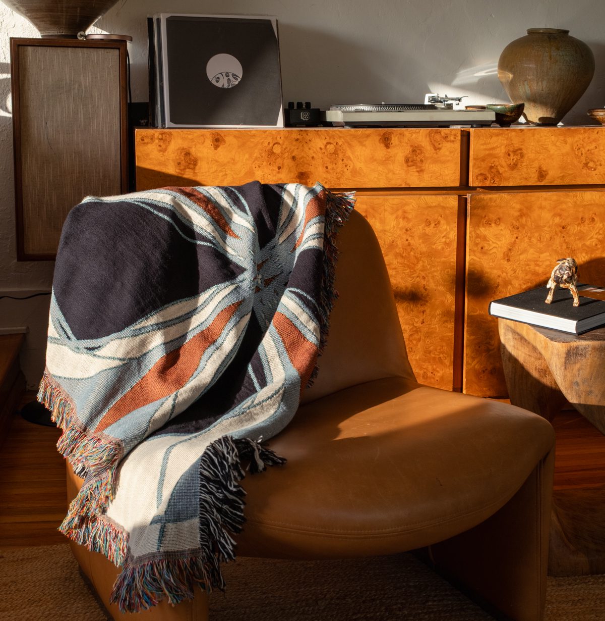 a brown leather chair with a woven thrown in front of a burl cabinet