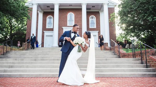 A married couple posts in front of the red brick and white columns of UMD's Memorial Chapel