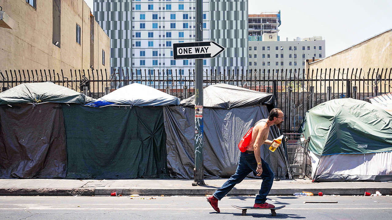 A man skateboards past a row of homeless tents on Skid Row in Los Angeles.