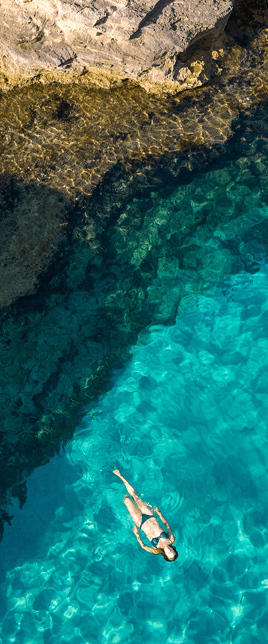 A woman floating in clear blue water near a rocky outcropping.