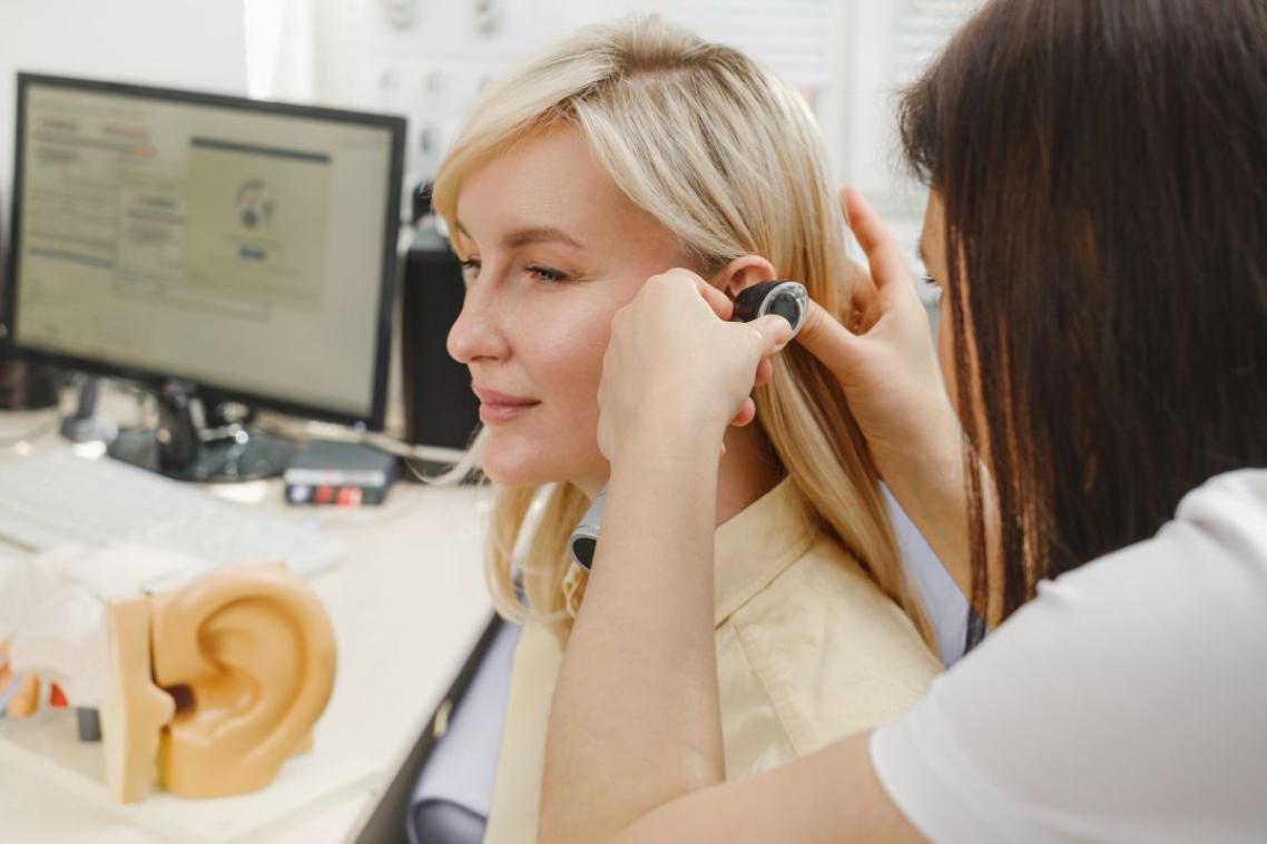Female patient having a hearing check up with a doctor examining her ear with an otoscope at a medical clinic.