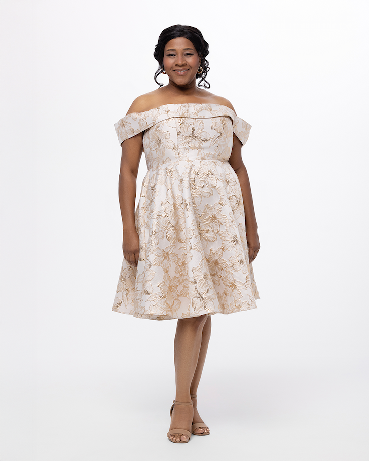 Woman wearing a short, cream and gold floral brocade dress.