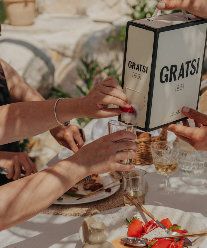 People pouring a glass of Gratsi White from the box at an outdoor dinner table.