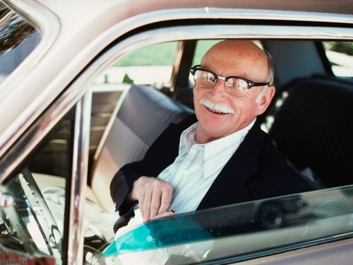 An elderly man sitting in the drivers side of a car.