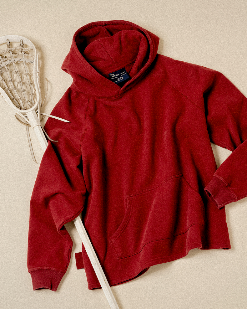 burgundy hoodie laid flat on light background next to field hockey stick