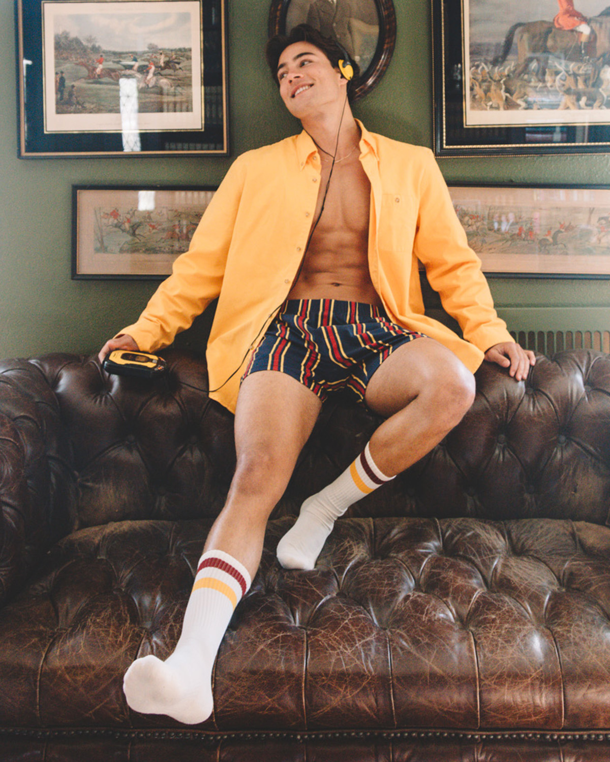 Man sitting on leather couch wearing yellow dress shirt, striped slim fit boxers and tech varsity classic crew socks with red/yellow stripes.