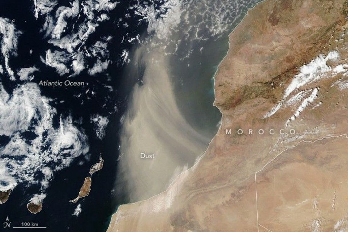 Satellite image of a large Saharan dust plume blowing westward from Morocco over the Atlantic Ocean, with the Canary Islands visible below the dust cloud.