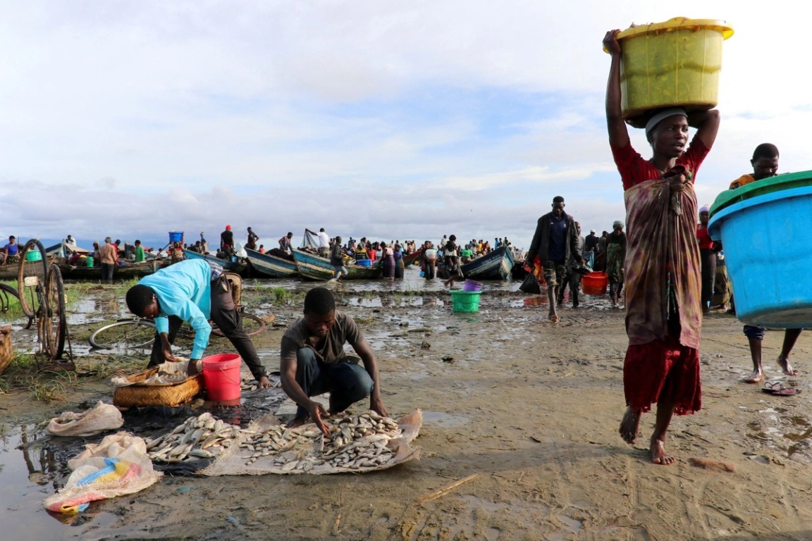 A woman carries a fish basket as she walks past fishermen sorting their catch on the shores of Lake Chilwa, near the border with Mozambique, in Malawi