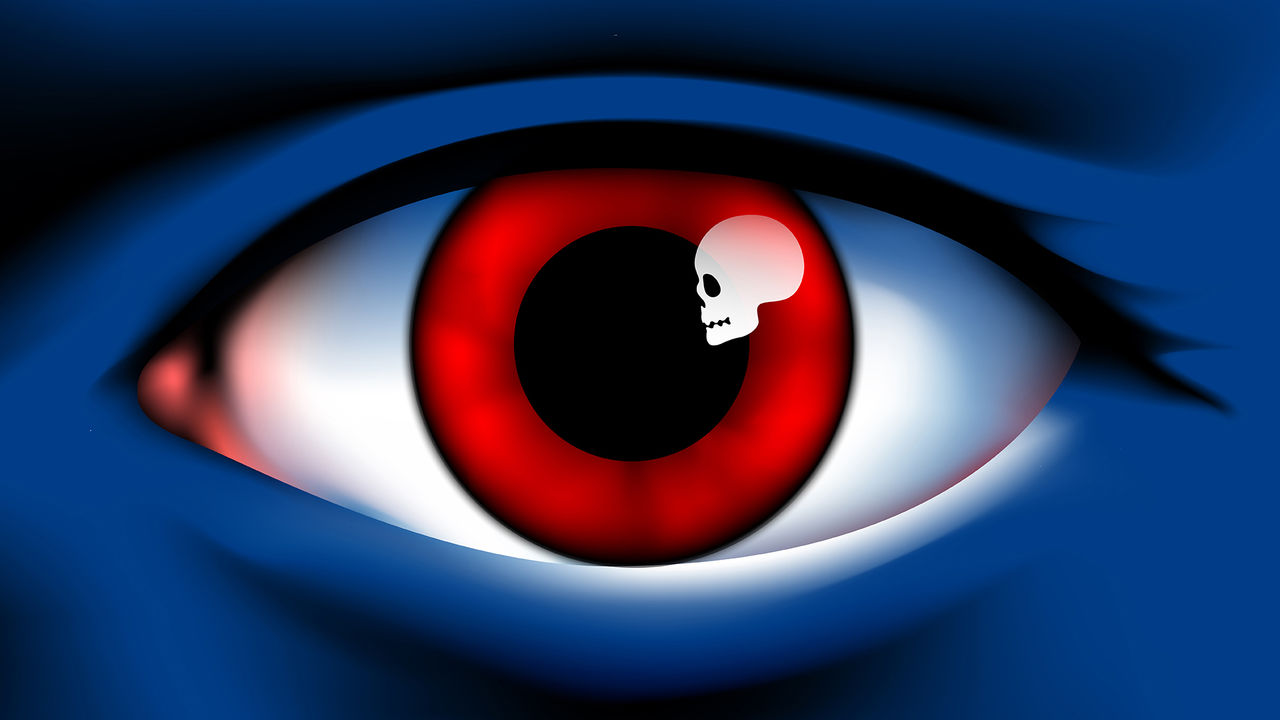 A close up eye with a red iris. The light reflecting in the pupil resembles a skull
