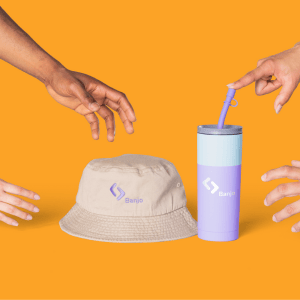 Four hands reaching for a custom bucket hat and a custom tumbler, on an orange background.