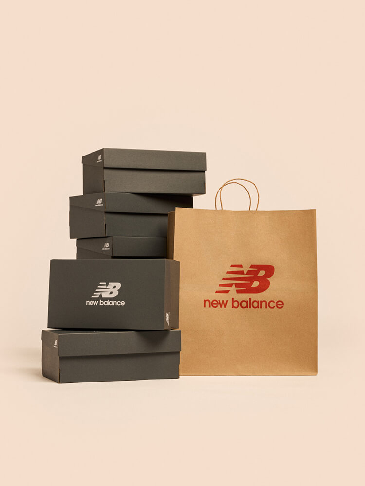 A stack of New Balance shoe boxes next to a shopping bag against a pale apricot backdrop