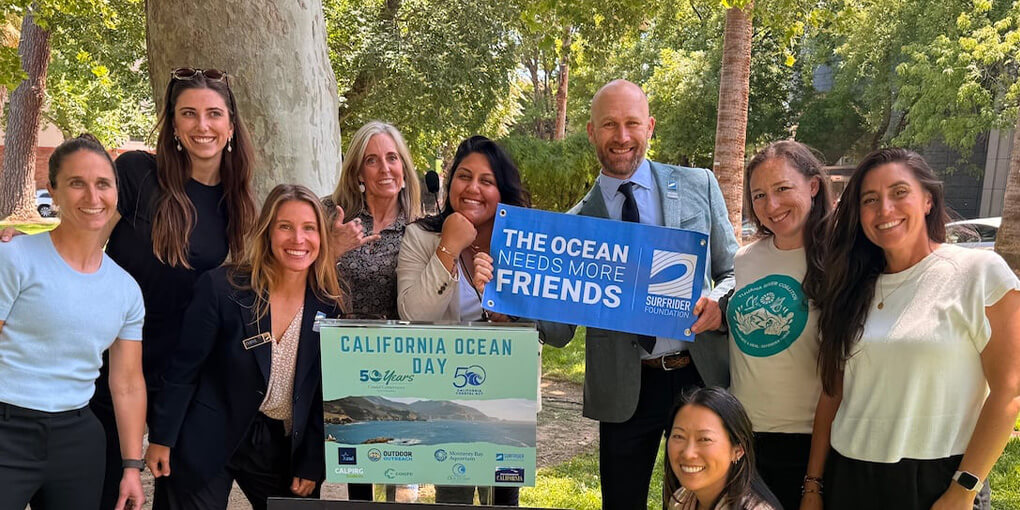 Nine Surfrider staff at California Ocean Day, holding a sign that reads, "the ocean needs more friends."