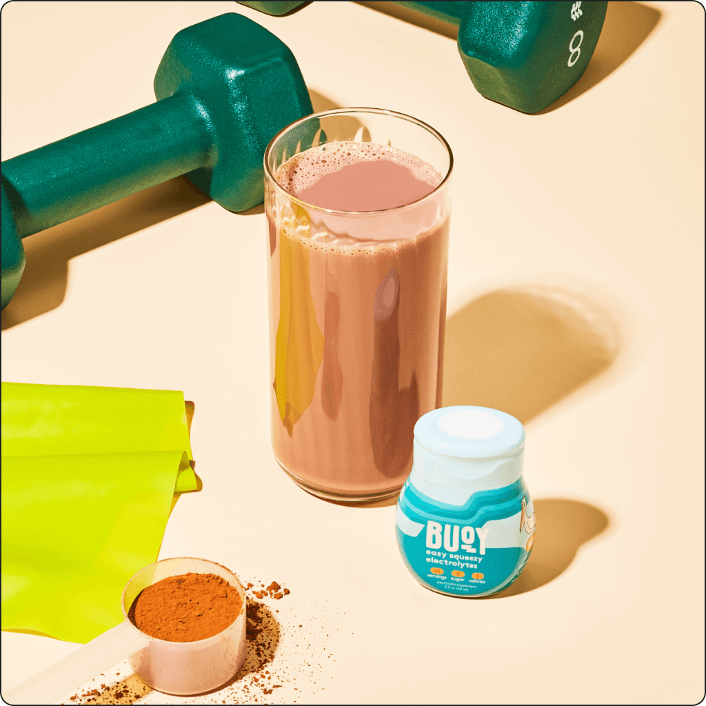 A bottle of Hydration Drops beside a protein shake and dumbbells.