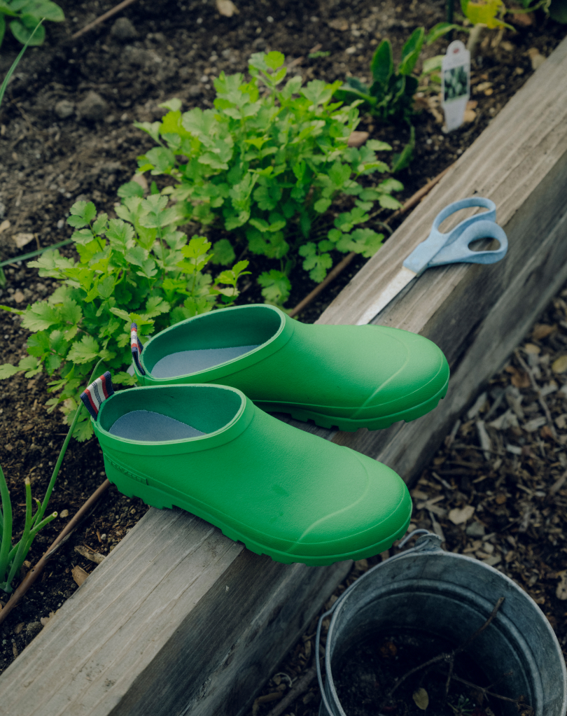 Green bodega clogs sitting on the edge of a garden bed