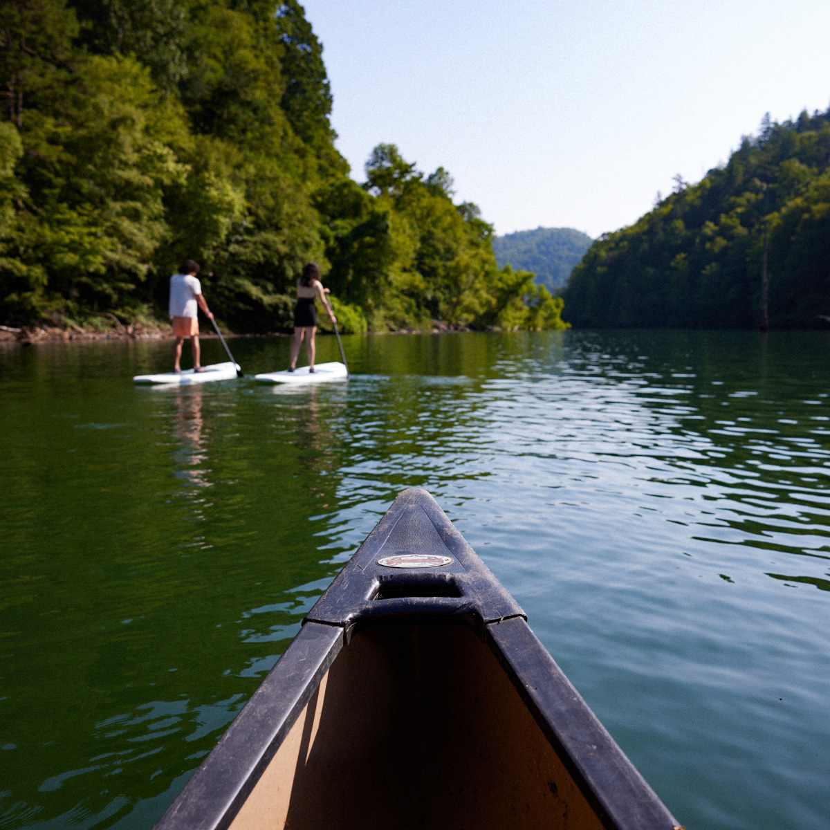 A photo from the bow of a canoe on a body of water with two paddle boarders ahead.