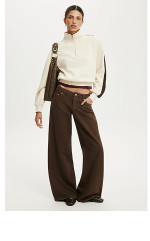 Model wearing cream cropped quarter-zip sweatshirt and brown wide-leg pants with brown shoulder bag