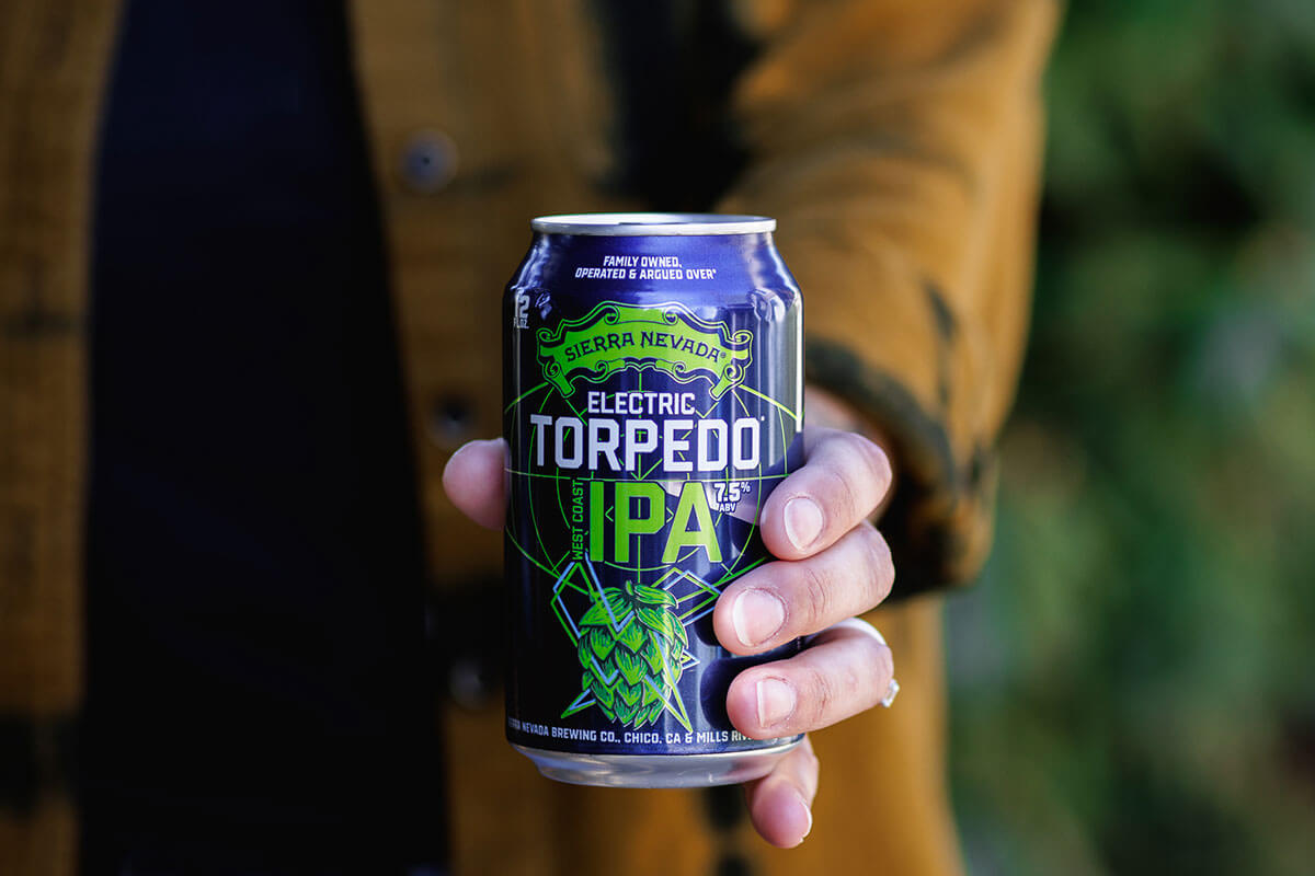 A hand holding out a can of Electric Torpedo IPA