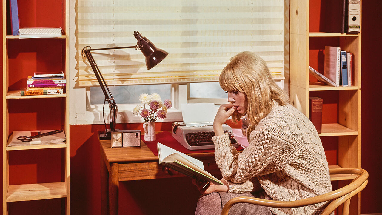 A woman reads a book at a desk in her home office