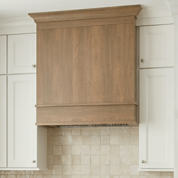 Wooden kitchen hood between white cabinets.
